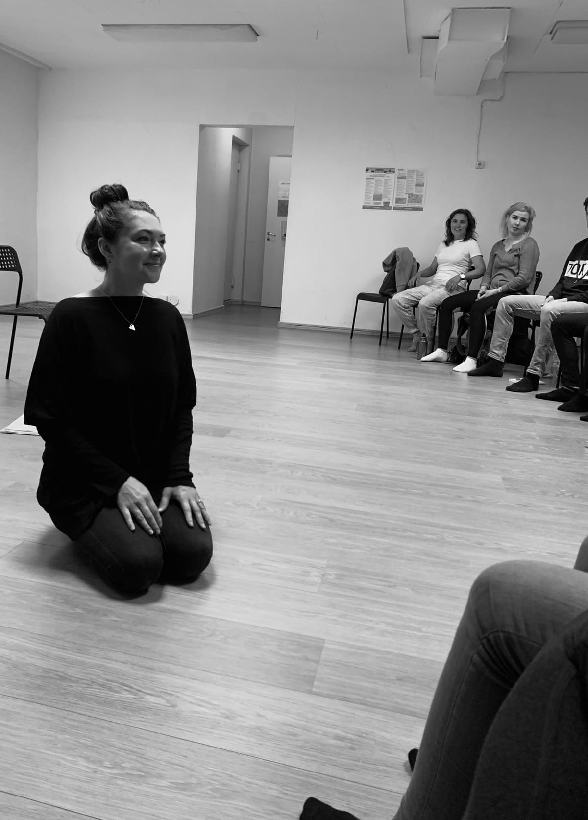 Black and white photo of Ashlie Walker kneeling at the front of an acting class