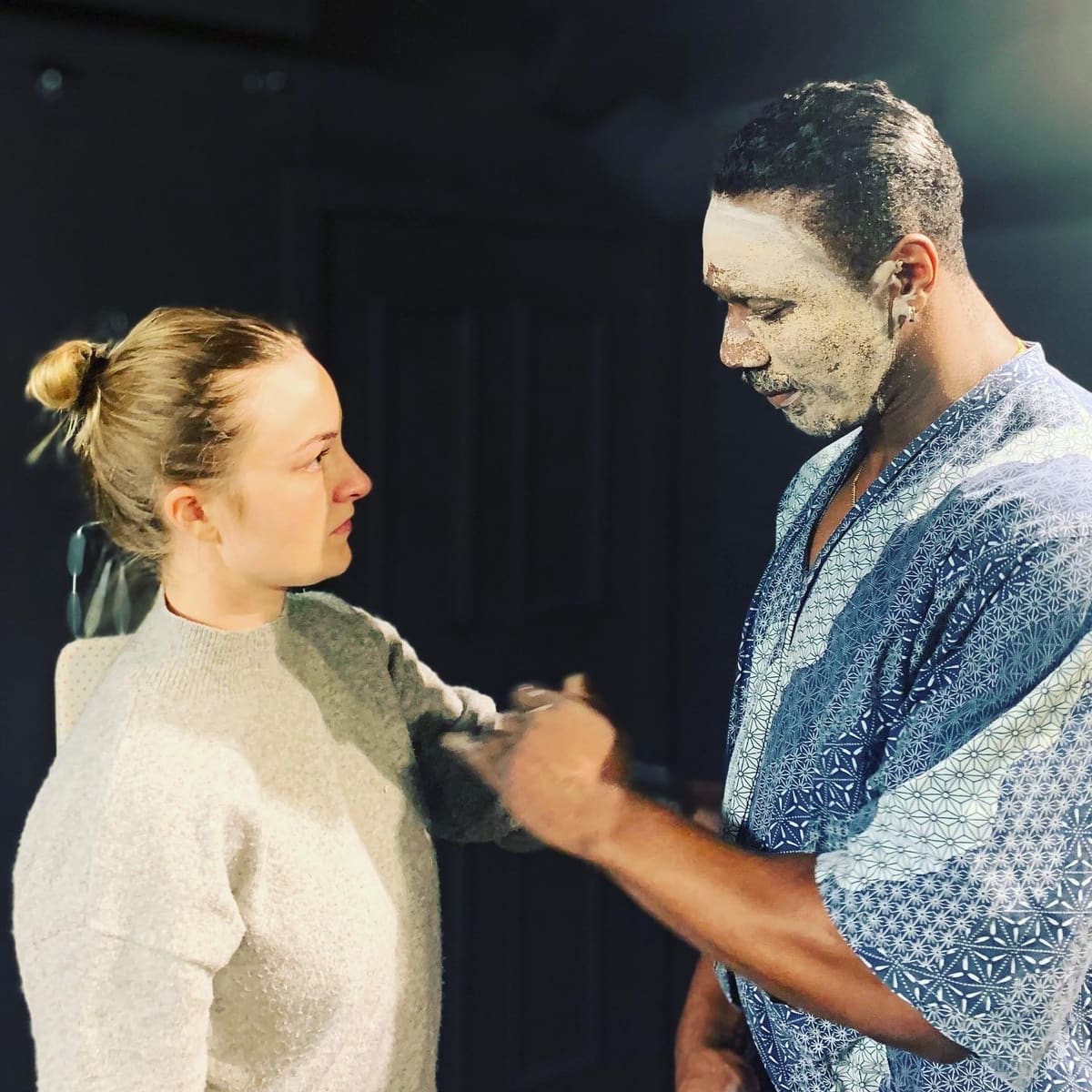 An actor applying face paint to a scene partner during rehearsal