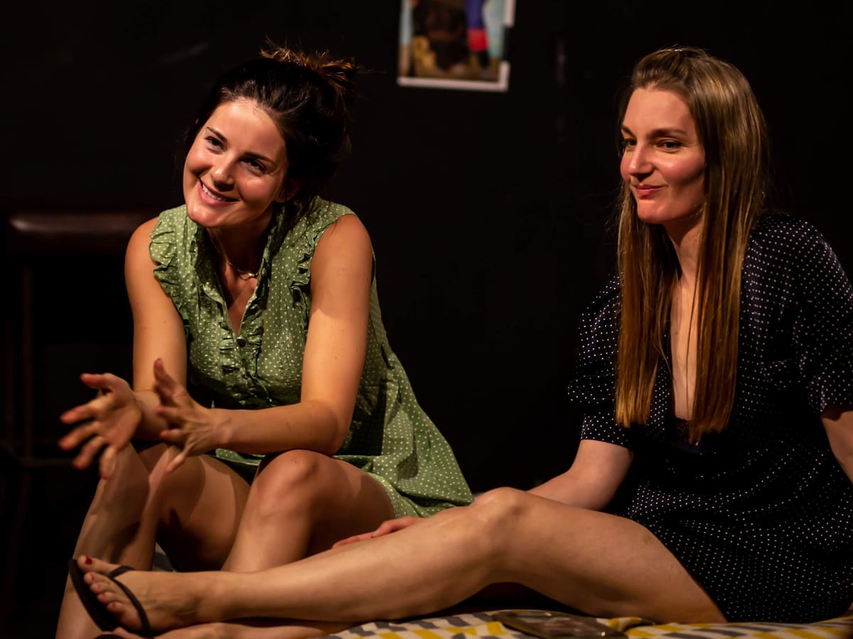 Two actors laughing together on a dimly lit stage during a scene study class